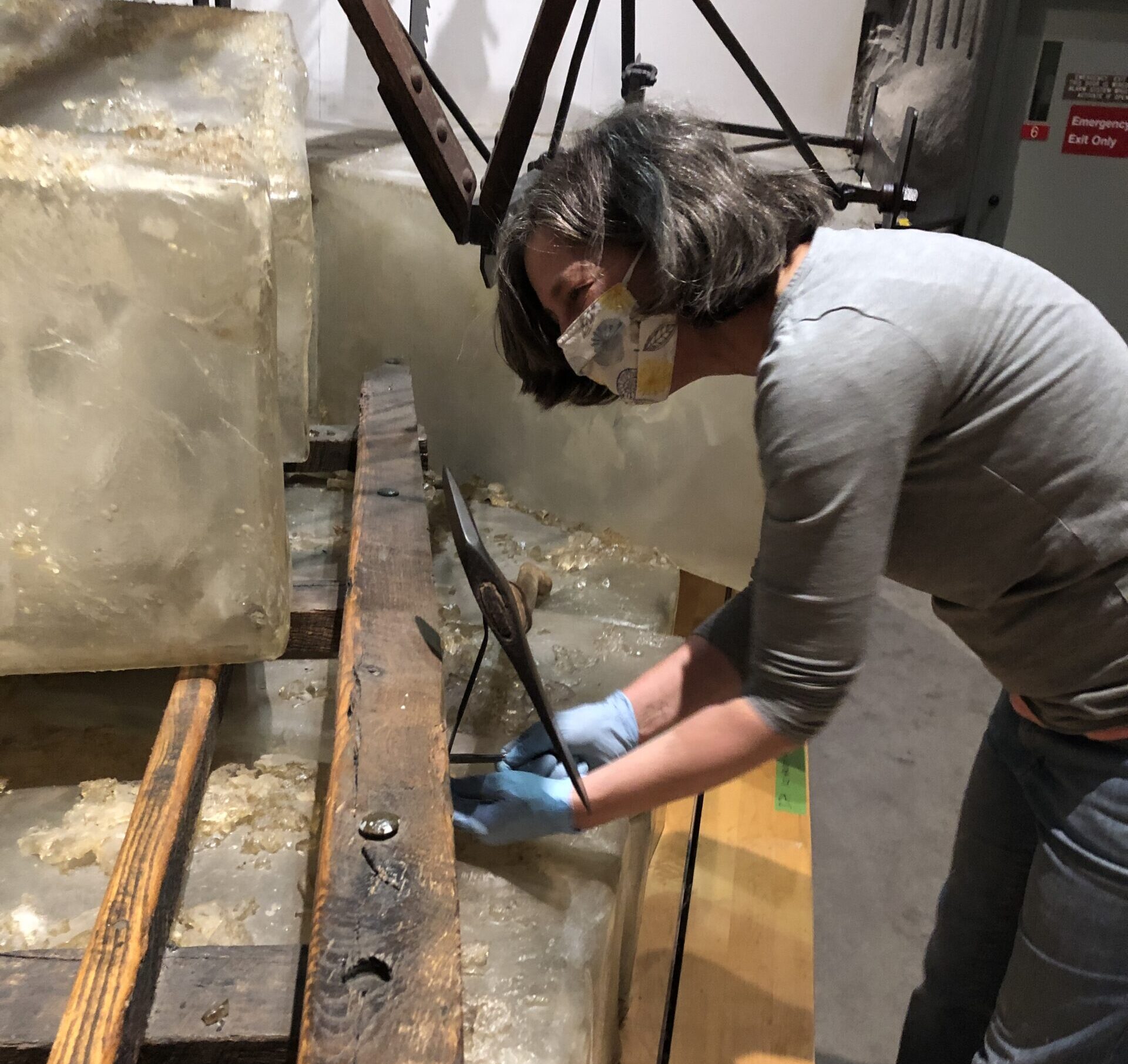 Woman in a mask and gloves moves a large block of ice in a museum exhibit.