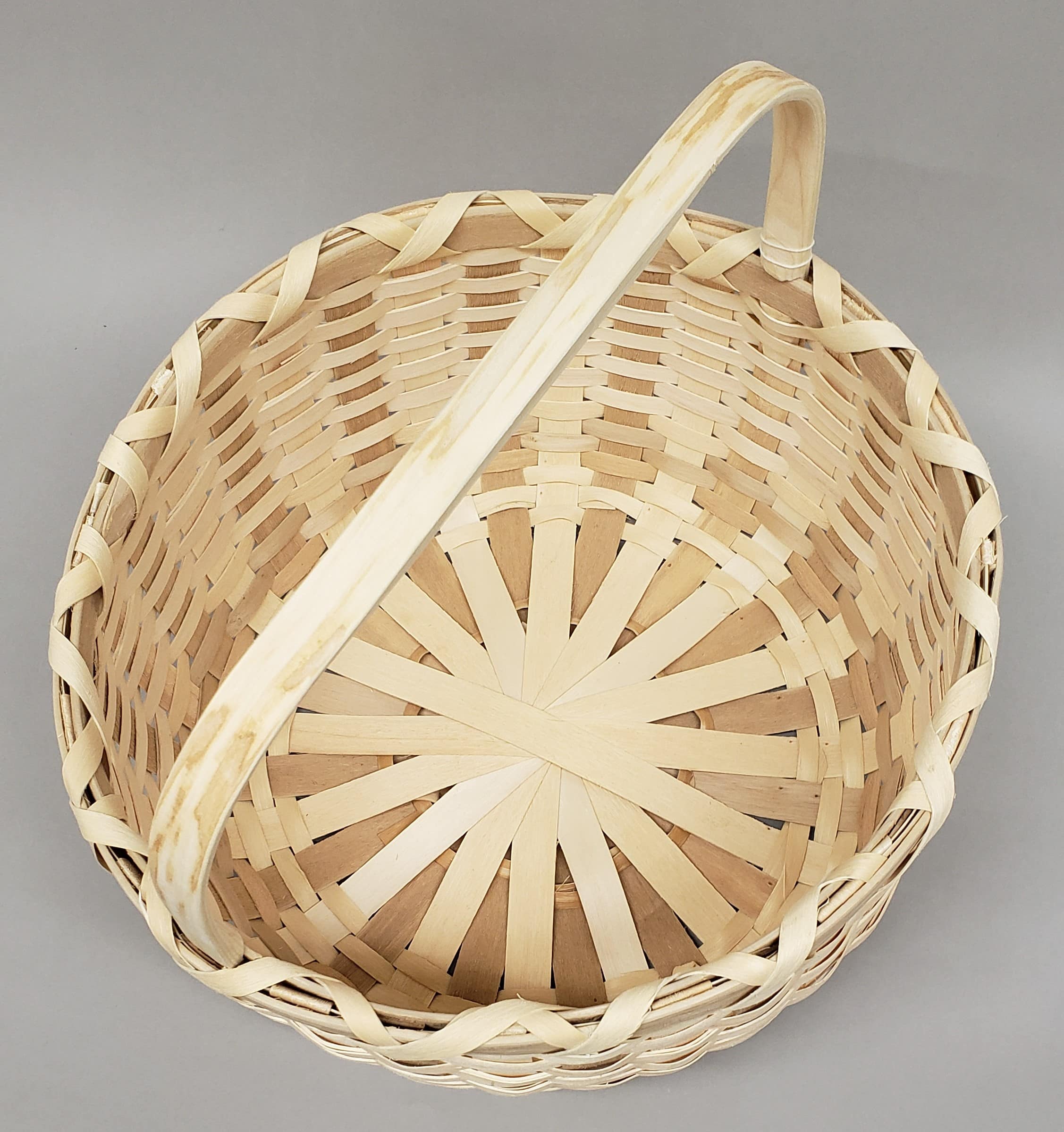 Top view of a round, woven wood basket with a handle on the top.