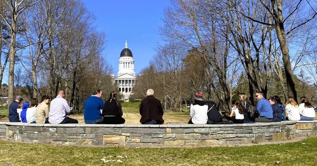 Group of people sitting on rock wall looking at state house