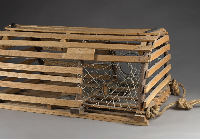 A wooden lobster trap is displayed on a gray background.