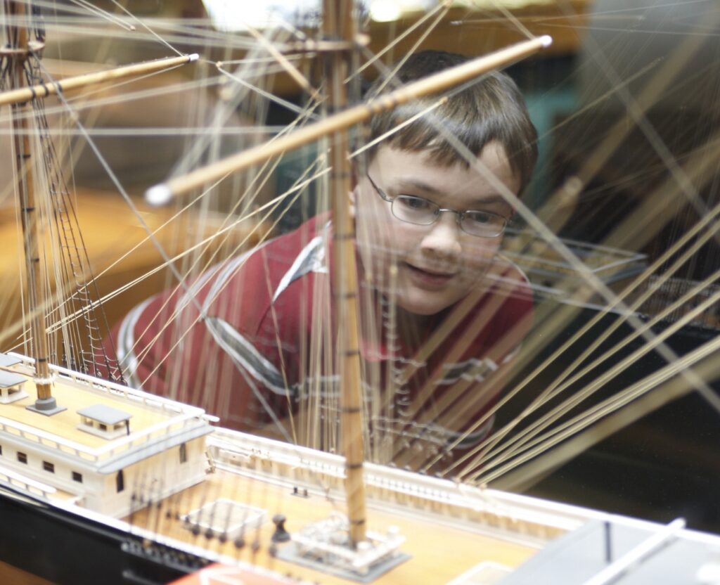 A boy gazes intently at a detailed model ship, admiring its craftsmanship and design.