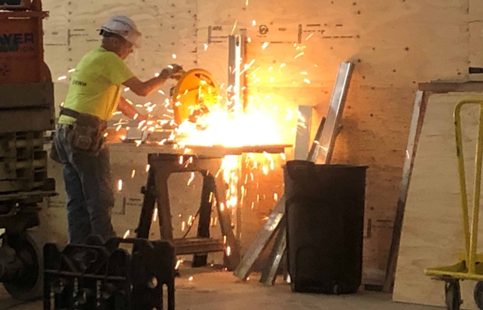 A man welds, creating bright sparks that fly from the wall, illuminating the workspace around him.