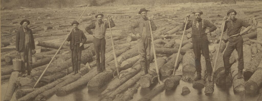 A group of men balancing on logs in the water.