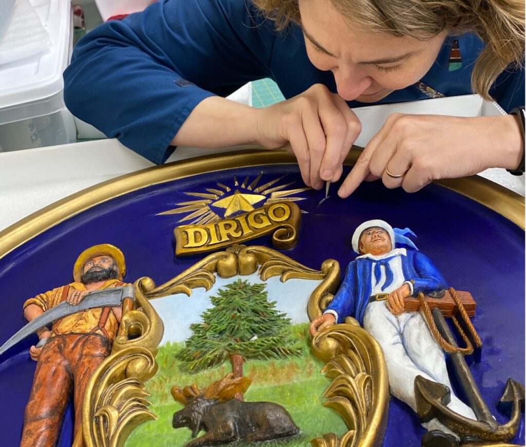 Museum staff doing detailed work on a Maine sign.
