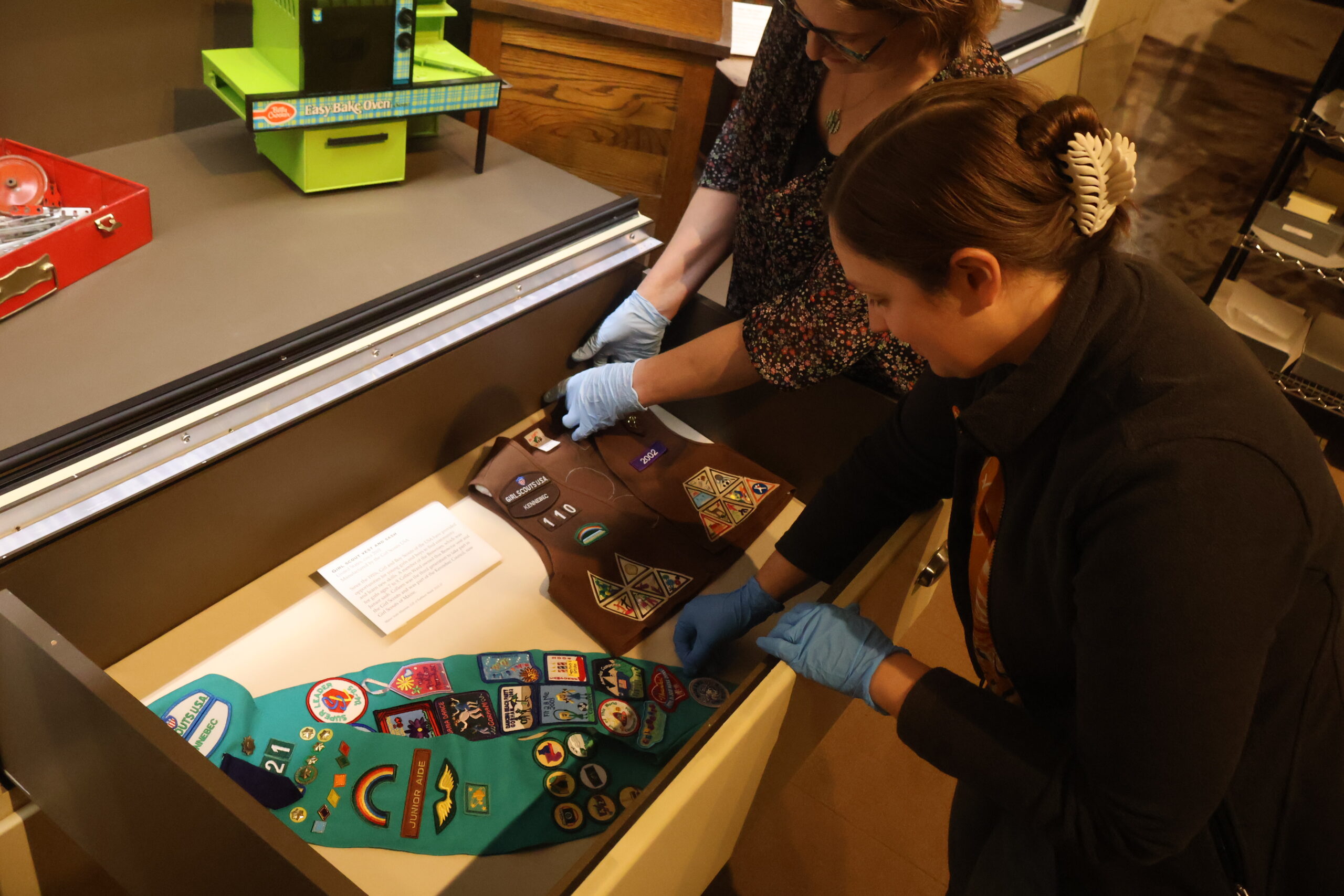 Two people carefully arrange vintage girl scout vests.